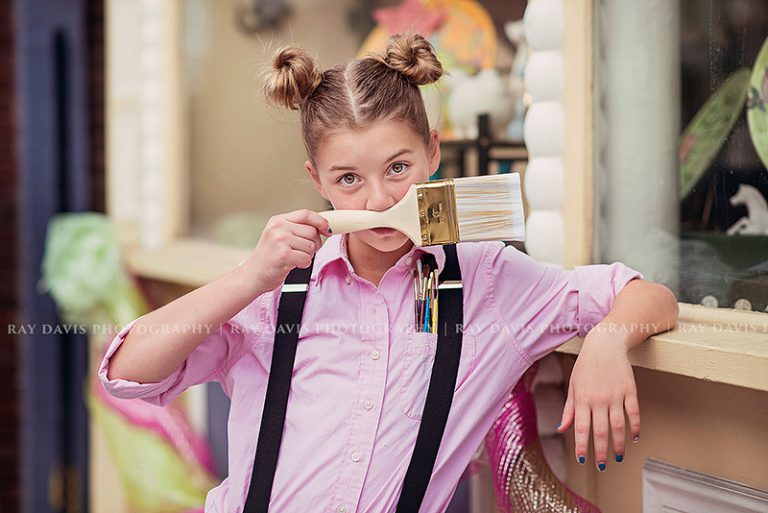 preteen girl using paint brush to make a mustache during louisville tween photo session with Ray Davis Photography